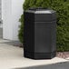 A black Commercial Zone PolyTec hexagonal waste container on a sidewalk.