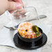 A hand using a Fineline Tiny Temptations black plastic lid to cover a small black container of shrimp.