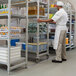 A man in a white coat and white hat standing in a warehouse next to Cambro Camshelving.
