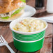 A green paper food cup filled with macaroni and cheese next to a sandwich.