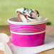 A pink and white striped paper cup filled with ice cream and sprinkles.