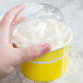 A hand holding a yellow Choice paper cup with white frozen yogurt in it.