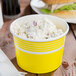 A yellow Choice paper cup filled with food.