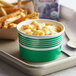 A close-up of a green and white Choice container with macaroni and cheese and french fries inside.