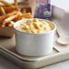 A tray with a bowl of macaroni and cheese in a white paper food cup with fries on a school kitchen counter.