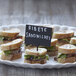 A plate of sandwiches with a mini chalk card pick sign on the table.