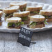 A plate of sandwiches on a table with American Metalcraft mini chalk cards in front of each sandwich.