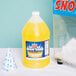 A close up of a Carnival King Pineapple Snow Cone Syrup bottle filled with yellow liquid next to a container of snow.