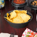 A round charcoal polyethylene basket filled with potato chips on a table with salsa.