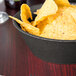 A charcoal polyethylene round basket filled with potato chips on a table.