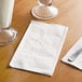 A white Choice 2-ply dinner napkin with a knife and fork on it on a table with a glass of milk.