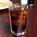 A GET Cubed clear plastic highball glass filled with brown liquid and ice with a straw.