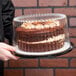 A person holding a chocolate cake in a D&W Fine Pack plastic cake container.