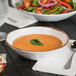 A GET Rustic Mill melamine bowl filled with soup and a salad on a table.