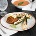 A GET Rustic Mill irregular round coupe plate with grilled vegetables and a bowl of soup on a table.