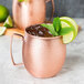A Clipper Mill hammered copper Moscow Mule mug with a drink, ice, and mint leaves.