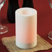 A white Sterno flameless pillar candle on a burlap napkin on a table with wine glasses.