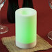 A white Sterno flameless candle with a green and white color changing flame on a table with wine glasses and a burlap napkin.