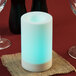A white Sterno flameless pillar candle with a blue light on a table with a red and black tablecloth.