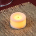 A lit Sterno white wax votive candle on a table with burlap cloth.