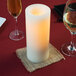 A Sterno cream flameless wax pillar candle on a table with wine glasses.