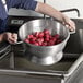 A person washing red potatoes in a Vollrath aluminum colander.