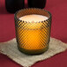 A Sterno green flameless wax filled glass candle holder on a table.