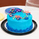 A close-up of a blue birthday cake with confetti on top in a D&W Fine Pack cake container with a clear dome lid.
