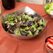 An American Metalcraft stainless steel bowl filled with salad and strawberries on a table.