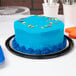 A blue cake with colorful sprinkles on a table in a clear display container with a clear dome lid.