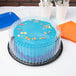 A blue cake with blue frosting and a clear plastic display cover on a table.