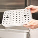 A person holding a Vollrath stainless steel tray with holes in it.