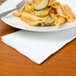 A plate of pasta and vegetables on a Hoffmaster white tissue dinner napkin with a fork.
