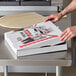 A person holding a white Choice pizza box on a counter.