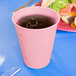 A Classic Pink plastic cup filled with a drink on a table next to a plate of food.