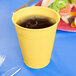 A close up of a Creative Converting Mimosa Yellow Plastic Cup with liquid in it.