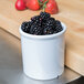 A white melamine round crock filled with blackberries on a counter.