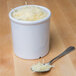 A white GET Melamine round crock filled with shredded cheese with a spoon.