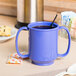 A peacock blue GET Tritan plastic two handle mug on a table with a spoon in it.