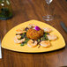 A GET Diamond Mardi Gras triangular yellow melamine plate with food on a table.