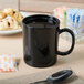 A black GET Tritan mug on a table with liquid in it.