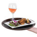 A hand holding a brown non-skid tray with a plate of food and a glass of wine.