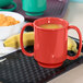 A black tray with a red Sensation mug filled with orange liquid and a bowl of cereal with a banana.