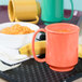 A Rio orange GET Tritan mug filled with orange liquid on a table with a bowl of food.