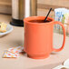 A GET Rio Orange Tritan mug filled with orange liquid with a straw on a table.