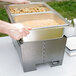 A person using a Sterno Silver Vein fold away chafer to prepare food on a table.