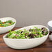 An Osslo ivory melamine bowl filled with salad on a table.