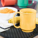 A yellow Tritan mug filled with porridge and a banana on a table.