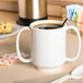 A white GET Ivory Tritan plastic two handle mug with brown liquid.