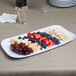 A white GET Siciliano melamine rectangular platter with fruit and crackers on a table.